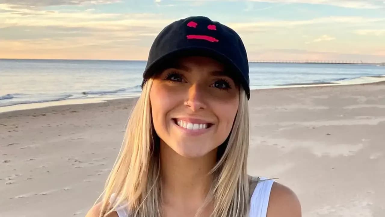 Emily Zugay smiling on a beach wearing a black cap with a red smiley face design, known for her viral logo redesigns on TikTok.