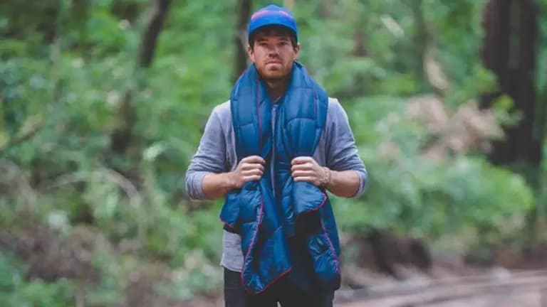 Wylie Robinson, founder of Rumpl, standing in a forest, wearing a blue Rumpl blanket around his shoulders.