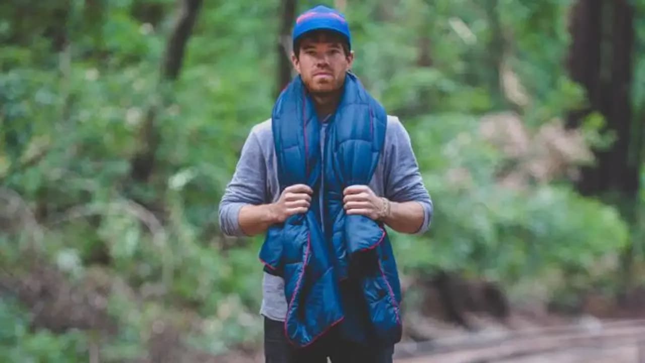 Wylie Robinson, founder of Rumpl, standing in a forest, wearing a blue Rumpl blanket around his shoulders.