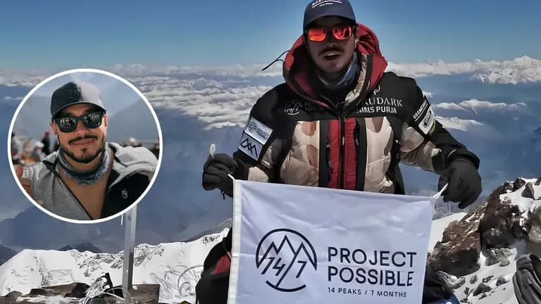 Nimsdai Purja holding a Project Possible flag on a snowy mountain summit with Himalayan peaks behind him.