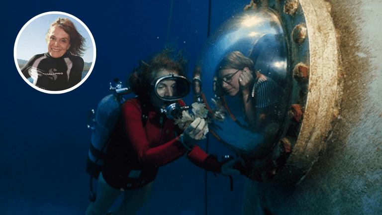 Sylvia Earle scuba diving during an underwater mission, showing coral to a researcher inside a habitat window