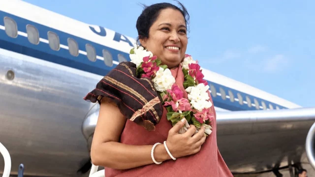 Colorized archival image of Shakuntala Devi wearing a flower garland beside an airplane