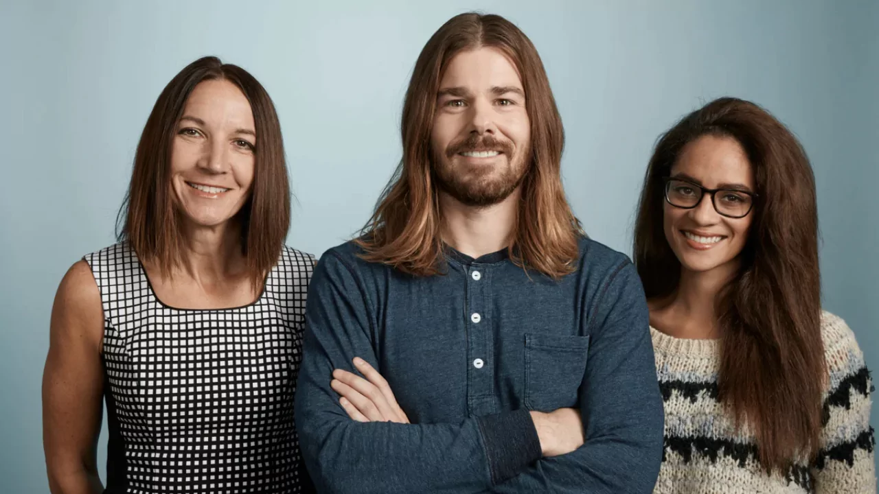 Dan Price, CEO of Gravity Payments, standing with two employees after taking a 94% pay cut to raise employee salaries to $70K.
