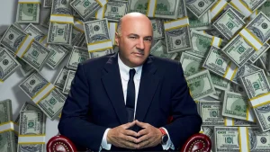 Kevin O’Leary sitting confidently in front of piles of cash, symbolizing wealth gained through smart investing rather than spending.