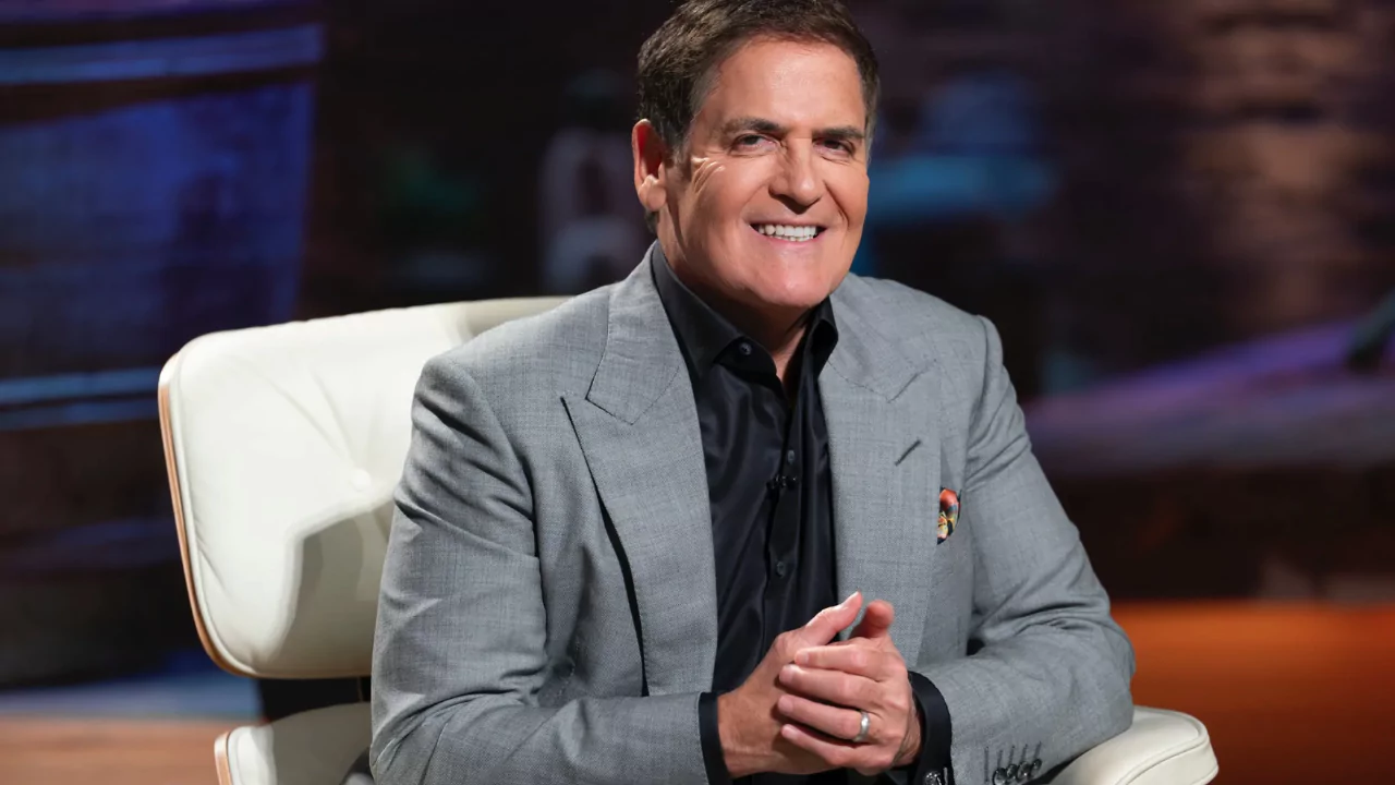 Mark Cuban smiling in a gray suit during a Shark Tank episode, known for investing in Relativity Space via cold email.