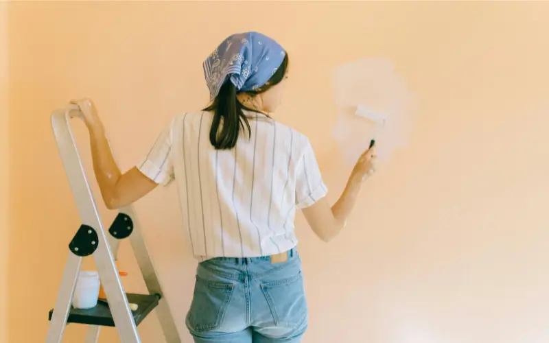 Woman painting a peach wall with a roller during a DIY home renovation project