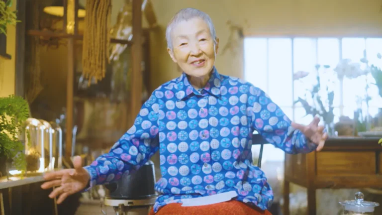 Masako Wakamiya, 87-year-old Japanese woman, smiling while seated in her cozy home studio. She became the world’s oldest app developer after building an iPhone app at age 80.