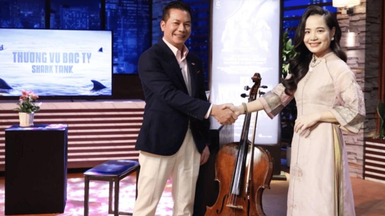 Dr. Đinh Hoài Xuân presenting Cello Fundamento on Shark Tank Vietnam, shaking hands with an investor beside a cello.