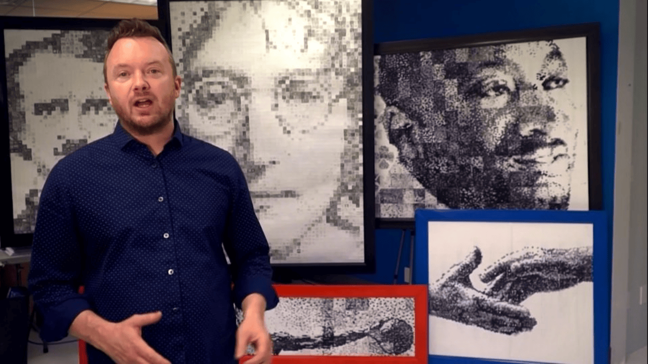 Phil Hansen standing in his studio surrounded by portraits he created using unconventional art techniques.